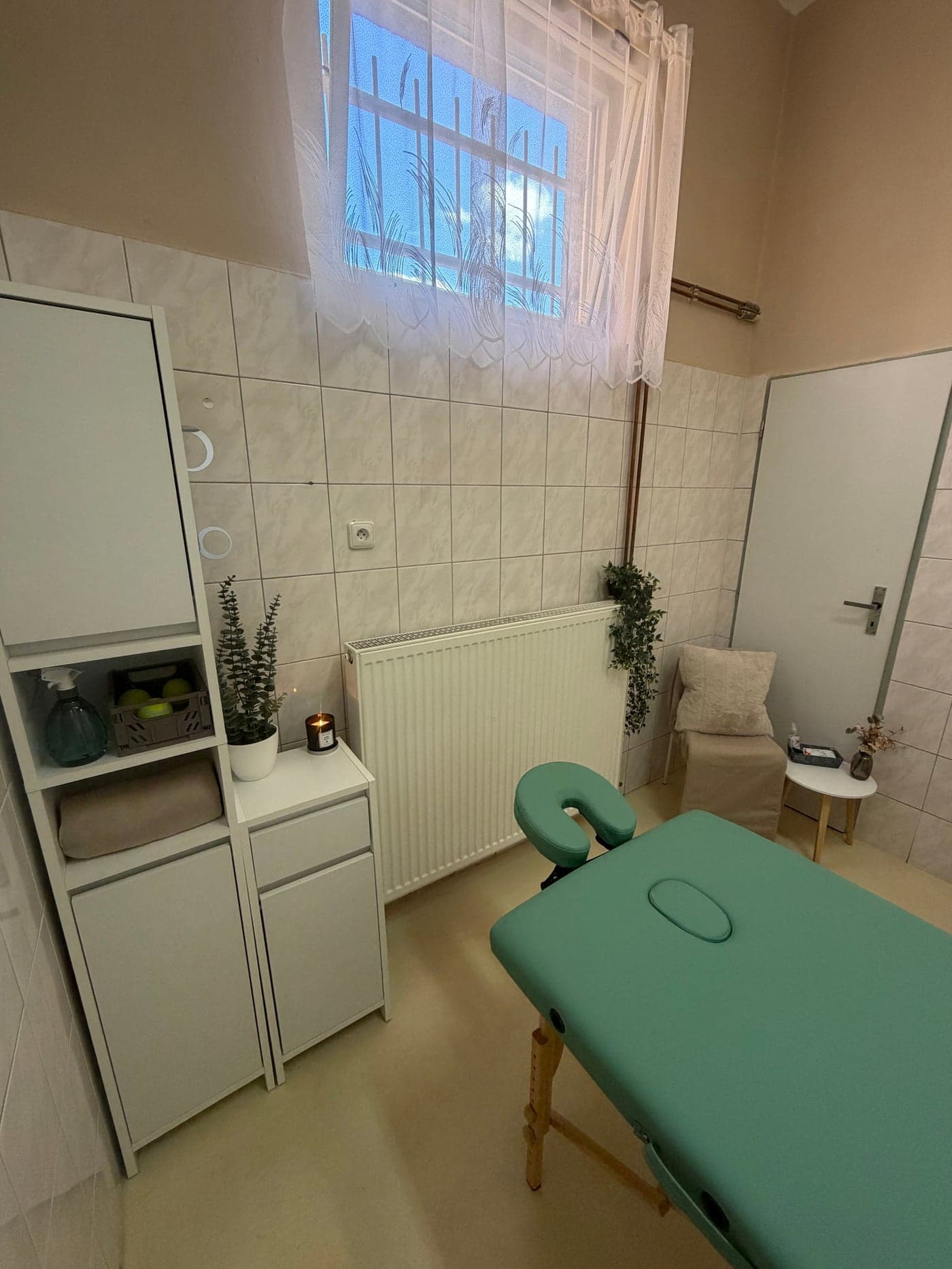 Masérna salonu Verona – zelený masážní stůl, skříňka s ručníky, svíčka a květiny